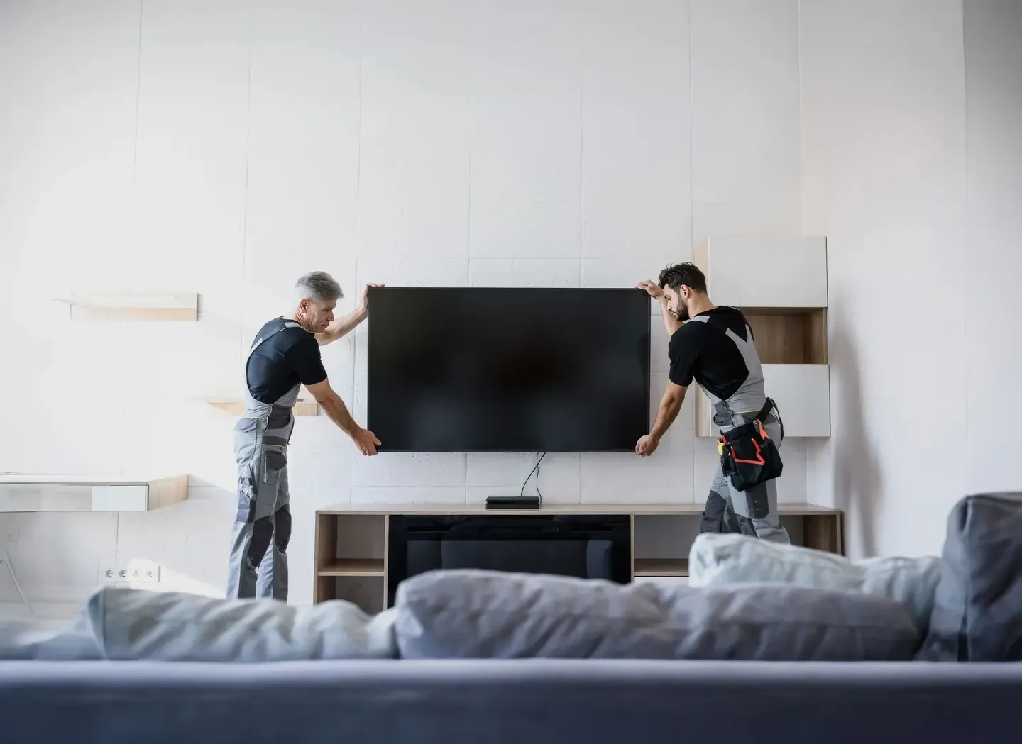Two TV Mount Master installers holding a television in a living room