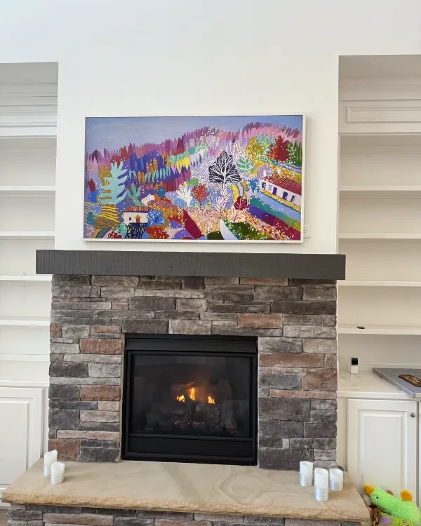 Frame TV showing a painting over a stacked-stone fireplace, white built-ins on both sides